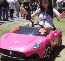 a woman is sitting in a pink toy car with the letter m on the front