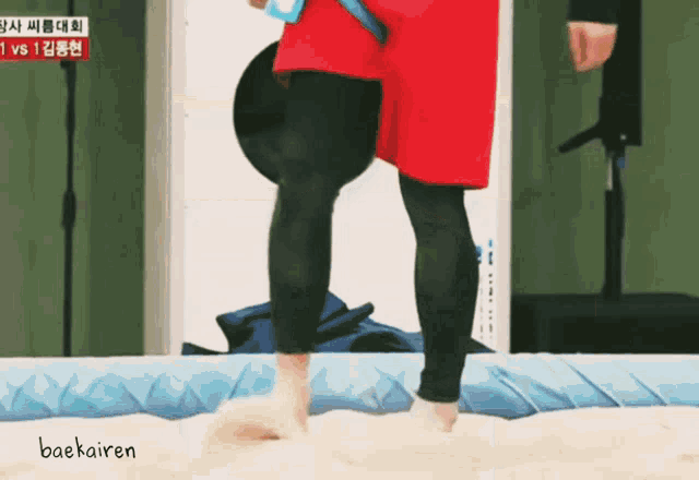 a person in a red shirt is standing on a sandy surface with the word baekairen written below them