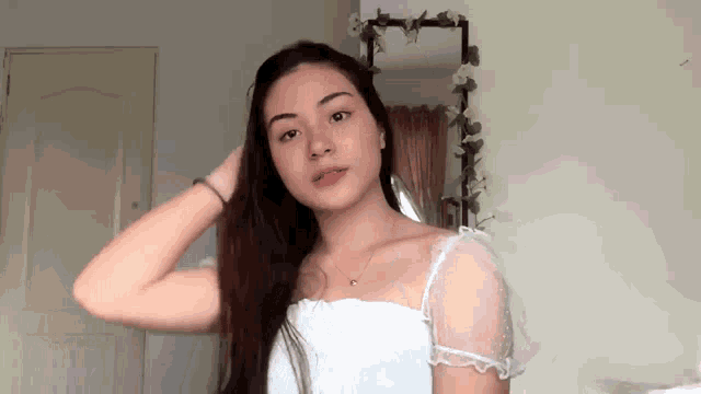 a young woman in a white top is standing in front of a mirror .