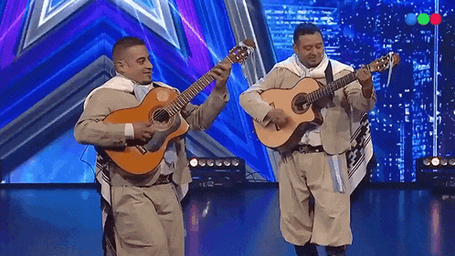 two men playing guitars on a stage in front of a colorful background