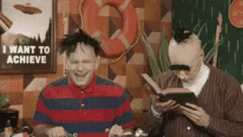 a man reading a book next to another man with a sign that says i want to achieve