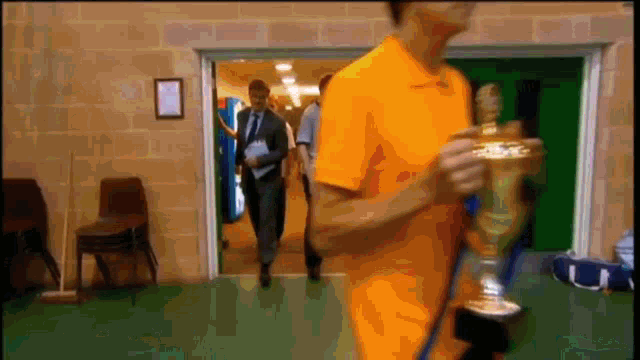 a man in an orange shirt is holding a gold trophy