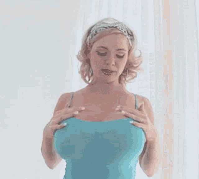 a woman in a blue tank top is standing in front of a window .