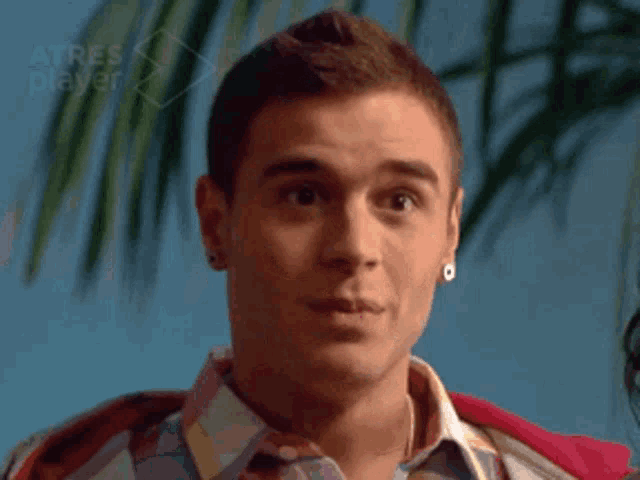 a man wearing earrings and a plaid shirt looks at the camera with the words atres player in the background