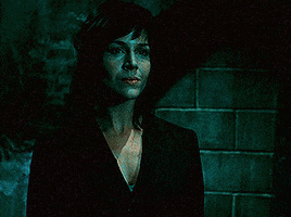 a woman in a black suit stands in a dark room