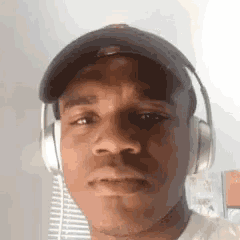 a young man wearing headphones and a baseball cap is looking at the camera .