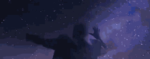 a man is standing in a dark room with his arms outstretched in front of a purple light .