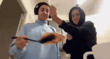 a couple of people are standing next to each other in a kitchen . one of the people is wearing headphones .
