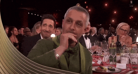 a man in a green jacket is sitting at a table with wine glasses and a sign that says n live