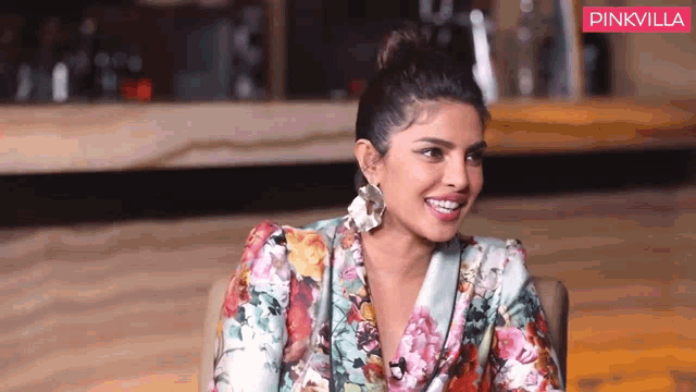 a woman wearing a floral jacket and earrings is smiling and sitting in a chair .