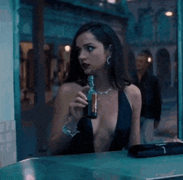 a woman in a very plunging black dress is drinking from a bottle that has the letter c on it