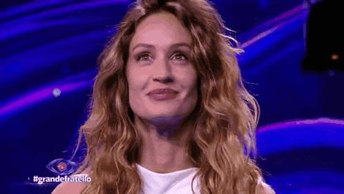 a woman with long curly hair is smiling in front of a blue background with the words grandechatello on it