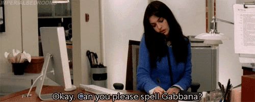 a woman sits at a desk with a computer and says " can you please spell gabbana "