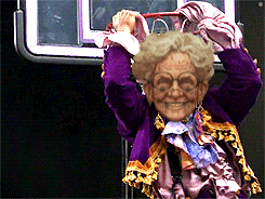 an elderly woman in a purple jacket is holding a cane over her head and smiling