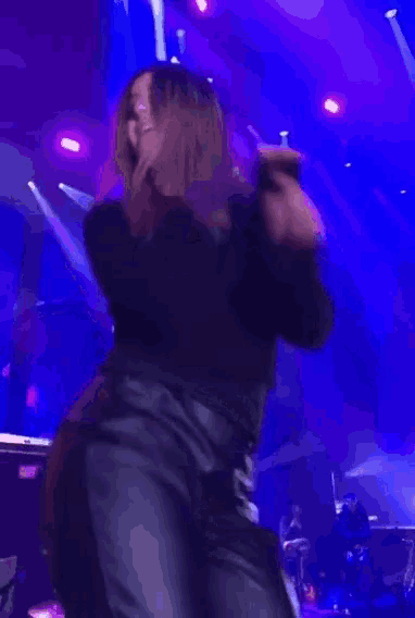a woman in leather pants is dancing on stage in front of a blue background .