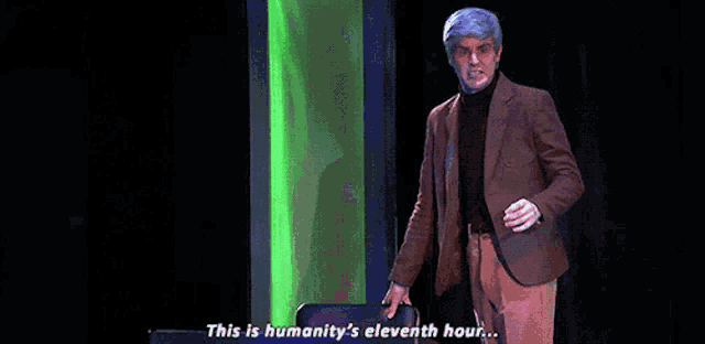 a man in a suit is dancing on a stage and says this is humanity 's eleventh hour ..