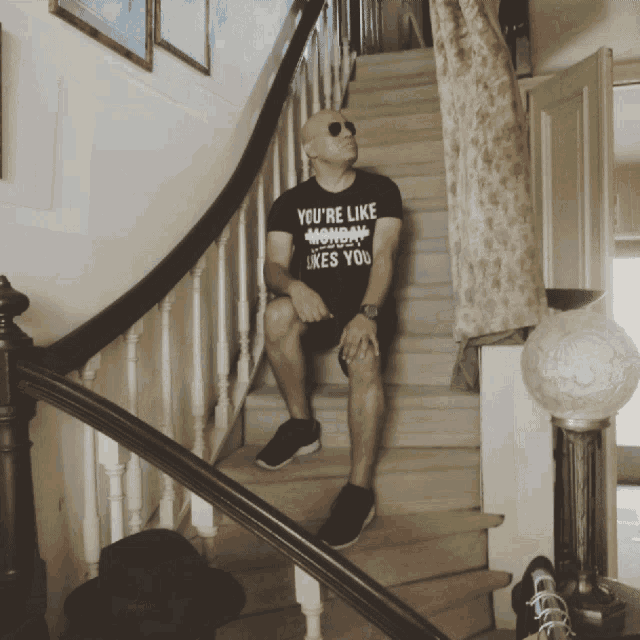 a man sits on a set of stairs wearing a black shirt that says you 're like monday likes you
