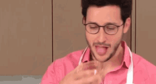 a man in a pink shirt and apron is wearing glasses and a pink shirt .