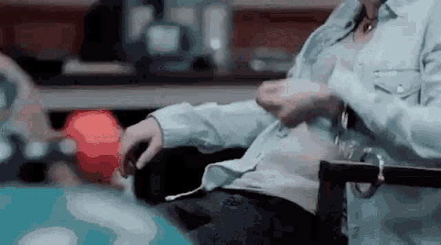 a man is sitting in a chair holding a bowling ball and looking at his shirt .