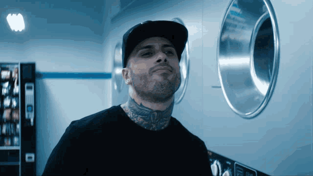 a man with a tattoo on his neck stands in front of a laundromat machine