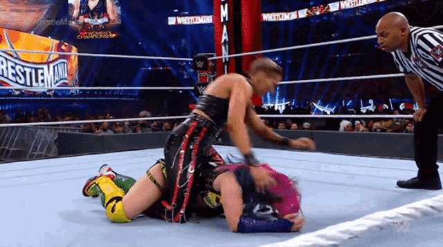 two women are wrestling in a wrestling ring and a referee is watching .
