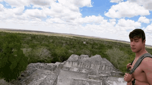 a shirtless man with a backpack is standing on top of a pyramid