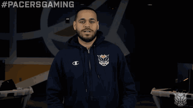 a man wearing a pacers gaming hoodie stands in front of a computer