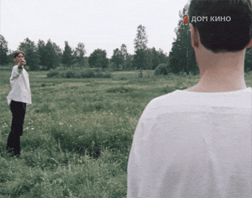 a man in a white shirt is pointing at another man in a field with a dom kino sticker on his head