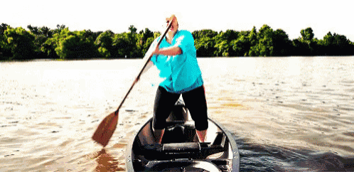 a man in a blue shirt is rowing a canoe on a lake