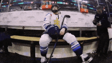 a hockey player sitting on a bench with a helmet that says ' bauer ' on it