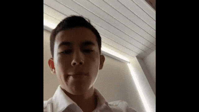 a young man in a white shirt is making a funny face while looking at the camera .