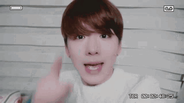a young man is giving the middle finger while wearing a white shirt and a blue sweater .