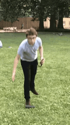 a man in a blue shirt and black pants is jumping in the air in a grassy field .
