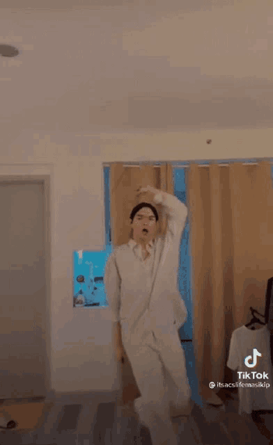 a man in a white suit is standing in a room with his arms in the air .
