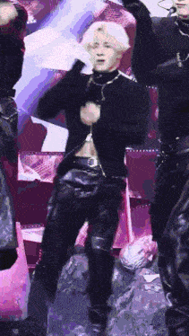 a man in a black jacket and leather pants is dancing on a stage with his hands in the air .