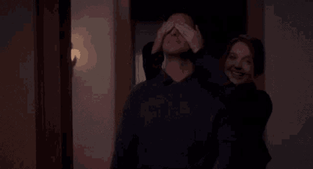 a woman is covering a man 's eyes in a hallway .