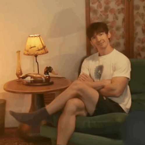 a man is sitting in a chair with his legs crossed in front of a lamp