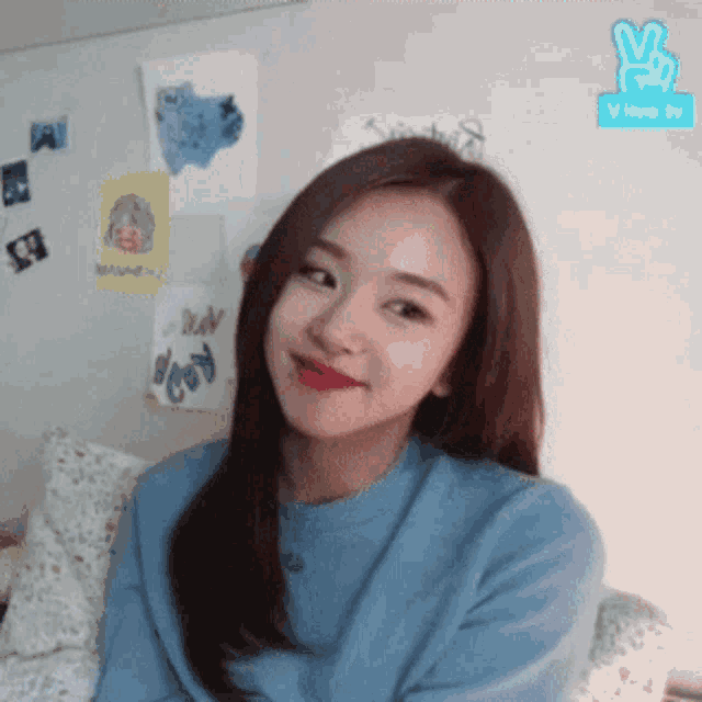 a girl in a blue sweater is sitting on a couch and smiling .