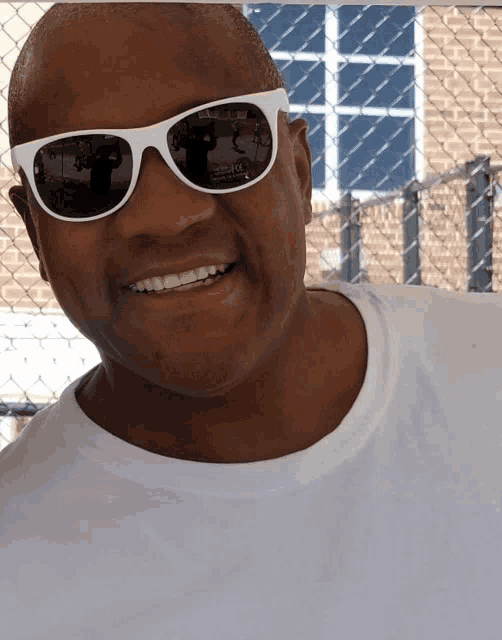 a man wearing a white shirt and white sunglasses smiles