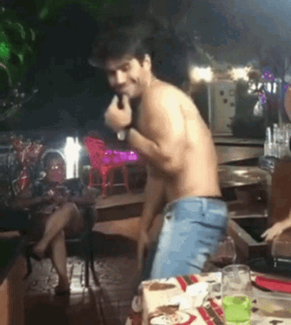 a shirtless man is dancing in front of a table with plates and glasses