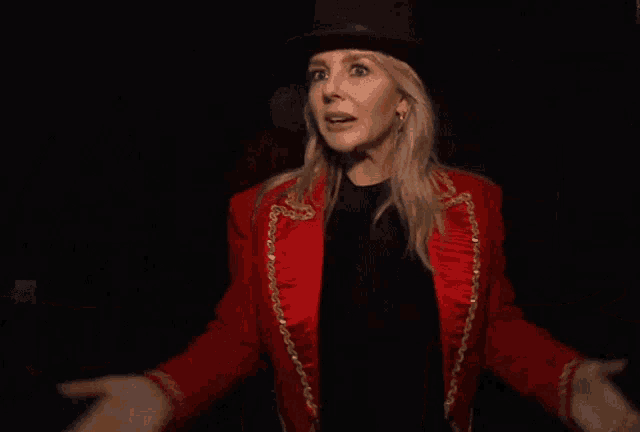 a woman in a top hat and red jacket is standing in the dark
