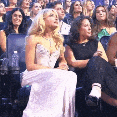 a woman in a white dress sits in a crowd watching a show