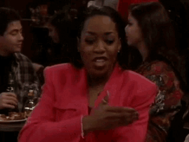 a woman in a red jacket is sitting at a table in a restaurant with other people .