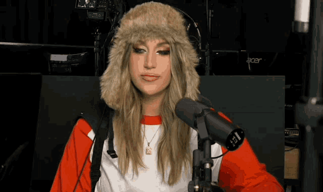 a woman wearing a furry hat and headphones is standing in front of a microphone .