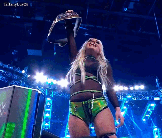 a woman in a green outfit is holding a championship belt in the air with the caption tiffanyluv24