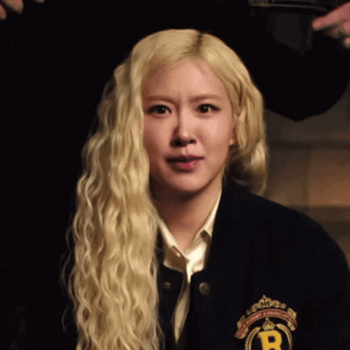 a woman with blonde hair is wearing a black jacket with the letter r on the front