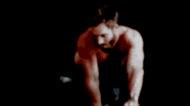 a shirtless man with a beard is flexing his muscles in a black background .
