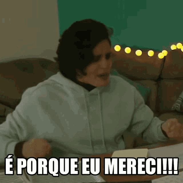 a woman sitting at a table with the words e porque eu mereci written on the screen