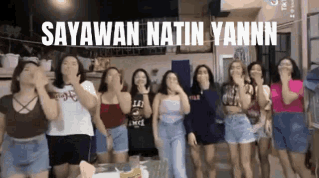 a group of young women are dancing in a room with the words sayawan natin yannn written above them .