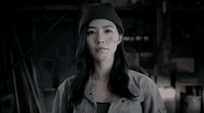 a woman wearing a beanie is standing in a dark room looking at the camera .